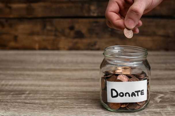 Man putting coin into donation jar on table, closeup. Space for text - Photo, image