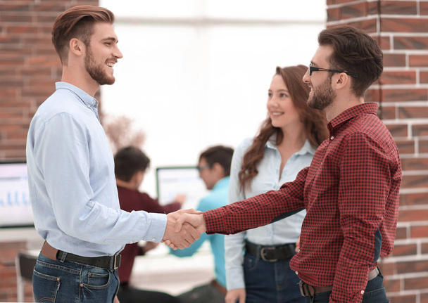 Smiling businessman shaking hands with colleague in office. - 写真・画像