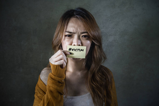 young sad and desperate Asian Korean student woman holding message paper as victim of abuse suffering domestic violence and bullying feeling helpless and harassed on isolated background - Zdjęcie, obraz