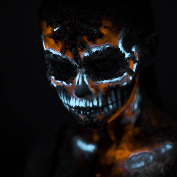 Πρόσωπο κοριτσιού βαμμένο σε φθορίζοντα χρώματα UV και μοιάζει με νέον λαμπερό κρανίο - Φωτογραφία, εικόνα