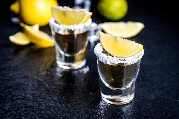 Tequila tradizionale messicana con limone, sale e cubetto di ghiaccio sul tavolo di pietra scura
 - Foto, immagini