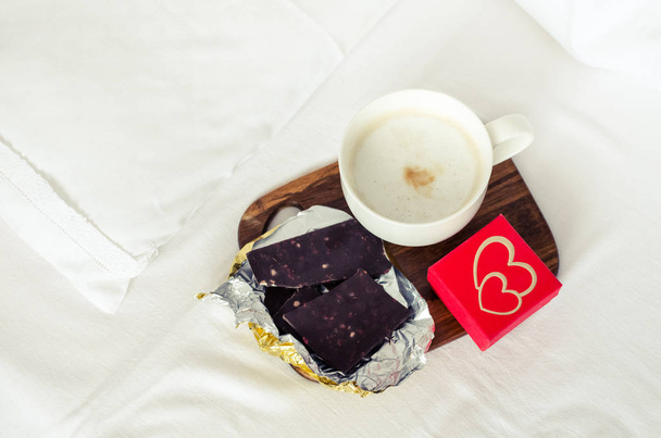 Romantic breakfast in bed. Coffee, dark chocolate and small present on white bed sheet. Concept Valentine holiday cozy warm home morning. - Φωτογραφία, εικόνα