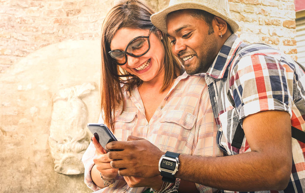 Multiracial couple using mobile smart phone at old town trip - Fun concept with alternative fashion travelers - Indian boyfriend with caucasian girlfriend on spring afternoon warm filtered look - Foto, afbeelding