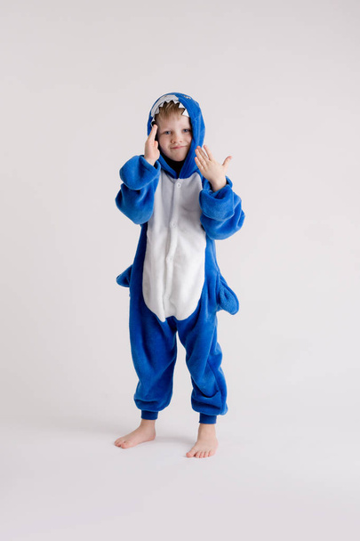 веселый маленький мальчик позирует на белом фоне в пижаме, в костюме голубой акулы
 - Фото, изображение