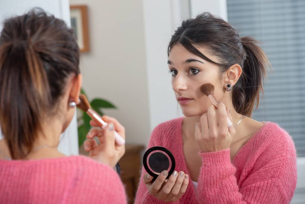 a young brunette woman putting makeup in the mirror - Fotoğraf, Görsel