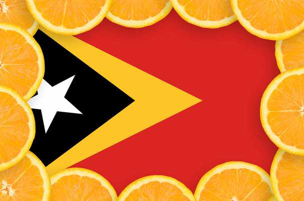 Timor Leste flag  in frame of orange citrus fruit slices. Concept of growing as well as import and export of citrus fruits - Photo, Image