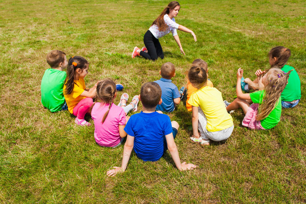 Takaisin näkymä lapset istuvat nurmikolla pelaa arvailuja
 - Valokuva, kuva