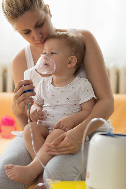Baby, das Atemtherapie einnimmt. Mutter mit der Maske eines Vernebelers - Foto, Bild