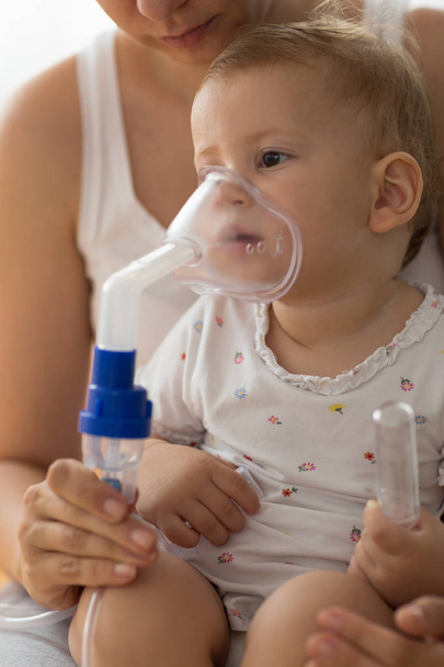 Baby taking respiratory inhalation therapy. Mother holding the mask of a nebuliser - Photo, image