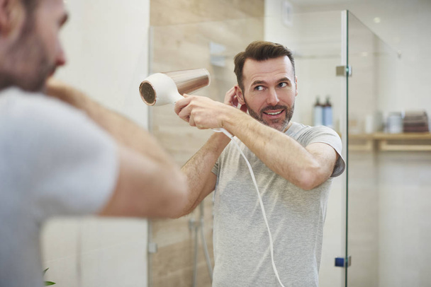 Homme souriant utilisant sèche-cheveux dans la salle de bain
 - Photo, image