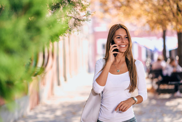 Smiling woman with mobile phone walking on the street. - Foto, Imagem