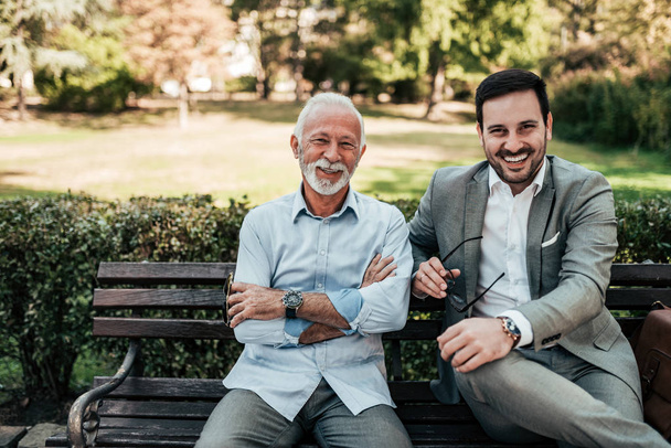 Portrait of a business family outdoors. Two men sitting in the park looking at camera. - Photo, image