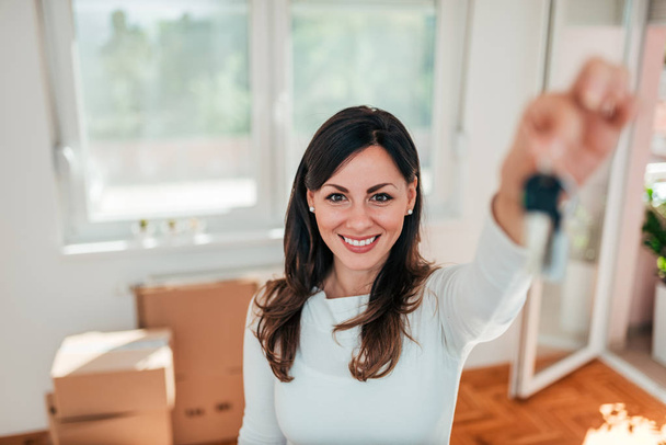Smiling young woman holding house keys of her new home. Real estate and relocation concept. - Foto, afbeelding
