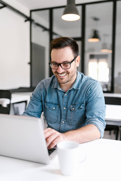 Smiling young man using laptop in modern office. - Fotoğraf, Görsel