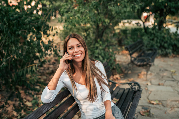 Beautiful woman sitting on a bench in the park, talking on the mobile phone. - Foto, Imagem