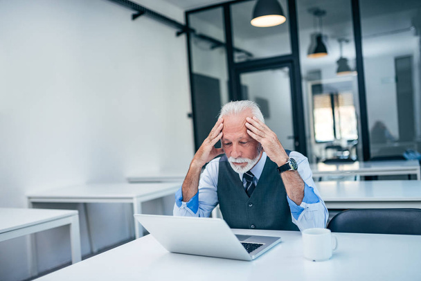 Worried senior business man holding head while looking at laptop. - Фото, изображение