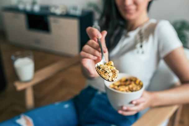 Close-up image of woman holding bowl of cereal and a spoon. Focus on the spoon. - Photo, Image