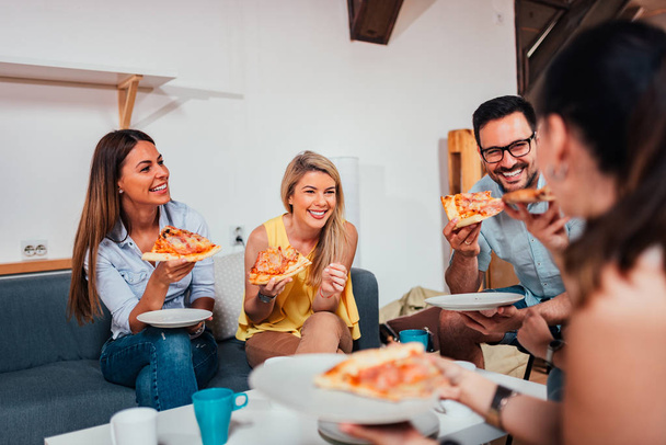 家庭でピザを食べながら笑っている友人のグループ. - 写真・画像