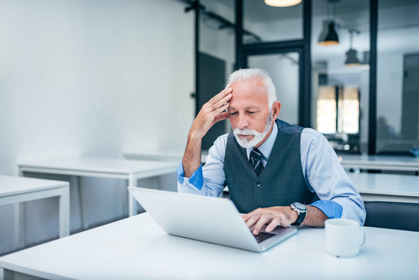 Worried senior businessman looking at laptop screen in modern office. - Фото, изображение