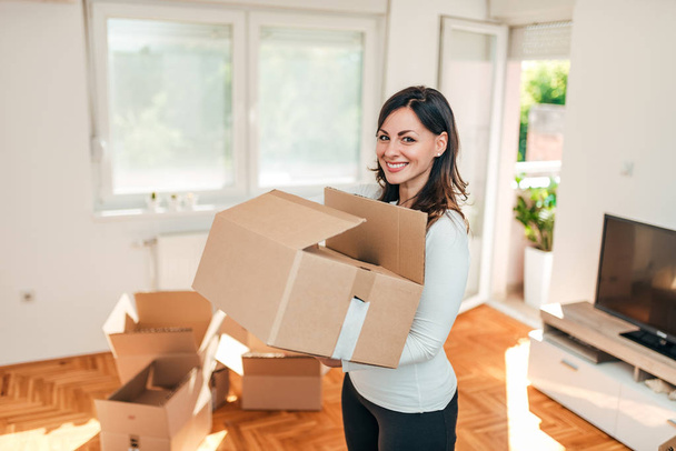 Cheerful young woman holding box. Moving day. - 写真・画像