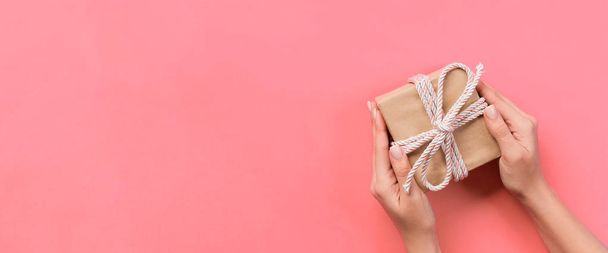 Жіночі руки, що тримають подарункову коробку з рожевою стрічкою на кольоровому фоні, банер верхнього виду з копією простору для вашого дизайну
. - Фото, зображення