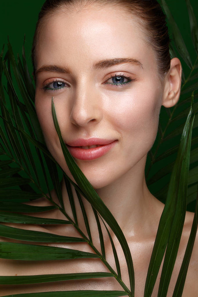 Beautiful fresh girl with cosmetic cream on the face, natural make-up and green leaves. Beauty face. Photo taken in the studio. - Foto, Imagem