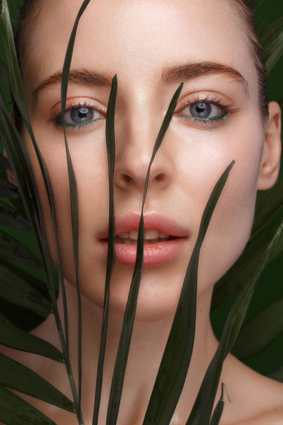 Beautiful fresh girl with cosmetic cream on the face, natural make-up and green leaves. Beauty face. Photo taken in the studio. - Foto, Bild