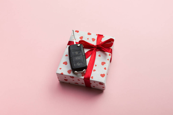 geben Geschenk Auto Schlüssel Konzept Draufsicht. Geschenkbox mit roter Schleife, Herz und Autoschlüssel auf korallenfarbenem Hintergrund. - Foto, Bild