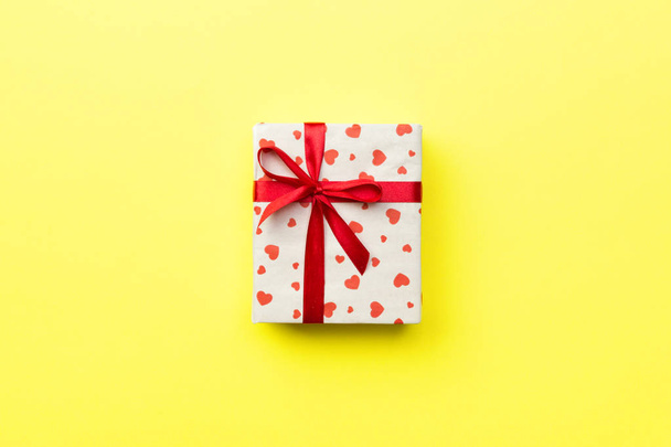 Gift box with red ribbon and heart on yellow background, top view with copy space for text. - Photo, Image