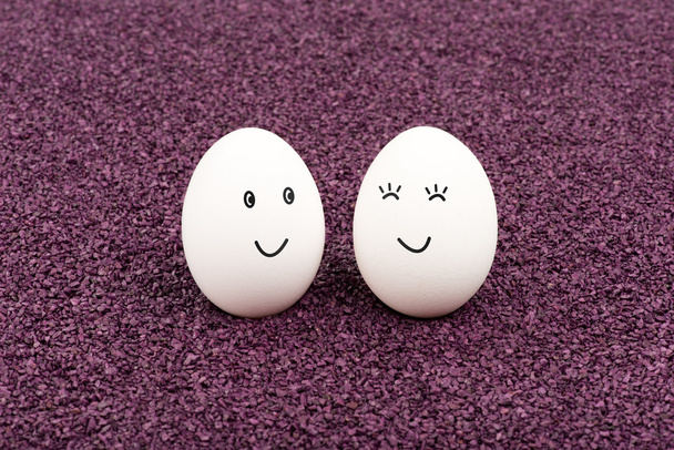 Dos huevos sonrientes sobre arena púrpura
. - Foto, Imagen