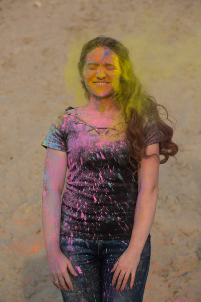 Felice donna bruna che si gode il festival Holi nel deserto. Donna in posa con esplosiva vernice gialla
 - Foto, immagini