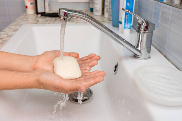 A gyermek kezében tartja a szappant, amelyen a víz áramlik a keverőből. - Fotó, kép