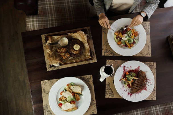 Set of dishes from: Caesar salad, grilled eggplant steak, vegetable salad with poached egg and "Striploin" steak in a wine sauce. Top view of woman having sitting at the wooden table - Fotó, kép
