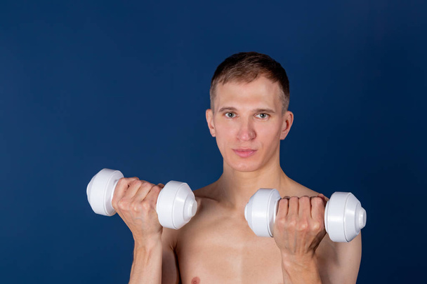 Closeup of a muscular young man lifting dumbbells on blue background - Foto, Bild