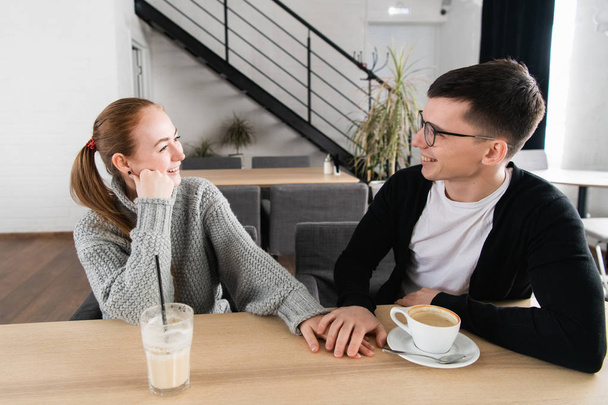 Foto de pareja joven y feliz tomados de la mano, mirándose y sonriendo mientras están sentados en el café
 - Foto, Imagen
