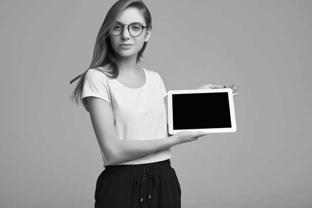 Portrait of cute teenage girl in white shirt and glasses holding digital tablet on gray background. Studio shoot. - Fotó, kép