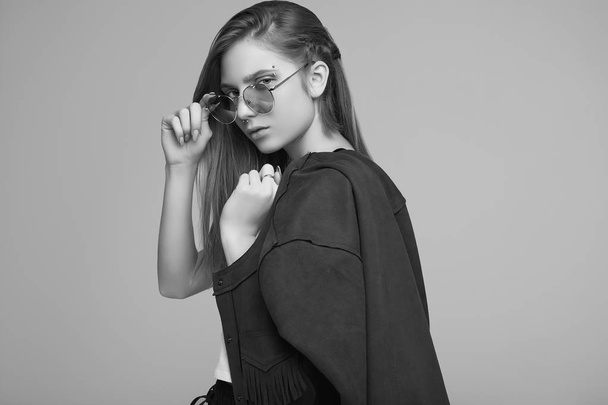 Retrato de linda adolescente en chaqueta de moda y gafas de color posando sobre fondo gris. Sesión de estudio
. - Foto, imagen