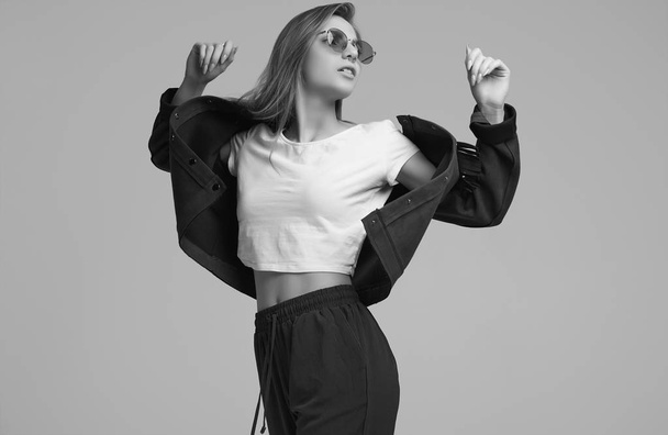 Portrait of cute teenage girl in fashion jacket and color glasses posing on gray background. Studio shoot. - Φωτογραφία, εικόνα