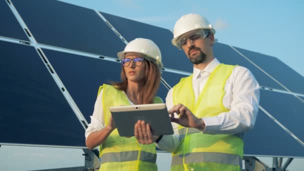 Close-up van twee werknemers staan in de buurt van zonnepanelen met een tablet. - Video