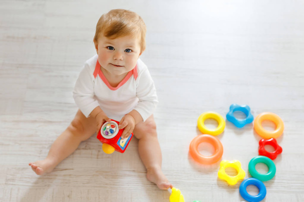 Bebek kız kreş eğitici oyuncaklar ile oynama. Mutlu sağlıklı çocuk evde renkli yumuşak oyuncaklar ile eğleniyor. Evlat plastik piramit inşa etmeye ve harflerle bloğu kullanma - Fotoğraf, Görsel