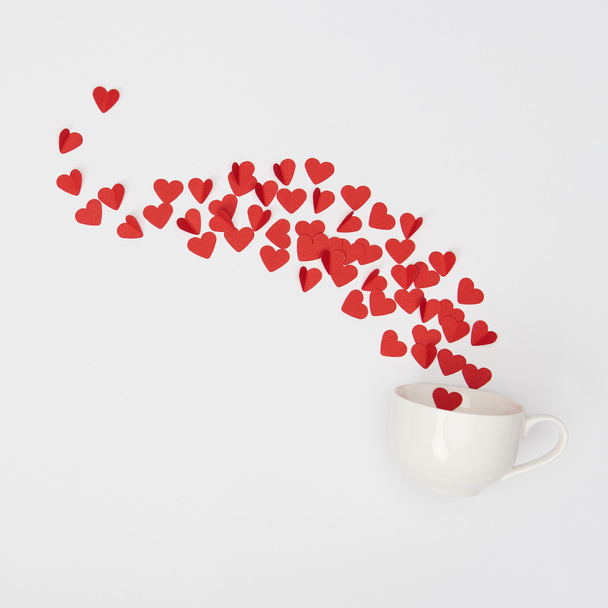 top view of cup and heap of red paper cut hearts on white background - Foto, Imagem