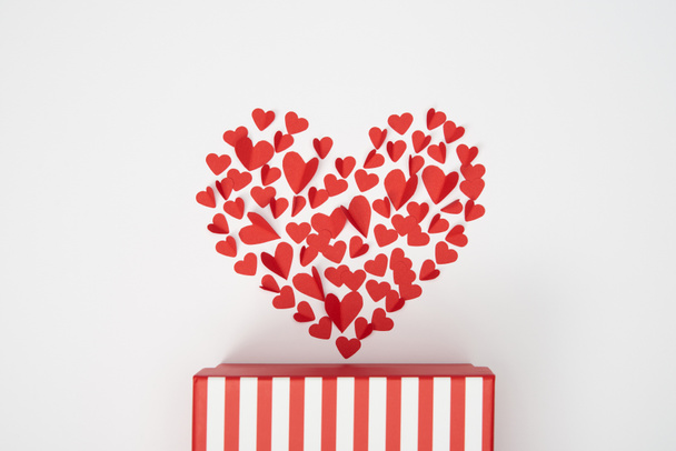 top view of heart shaped arrangement of small red paper cut hearts and striped gift box on white background - Photo, image