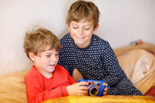 Deux enfants d'âge préscolaire ou scolaire garçons, frères et sœurs et frères s'amusent après l'école en jouant à un jeu vidéo à la maison et en prenant des photos avec un appareil photo jouet. Meilleurs amis, jumeaux en pyjama ou vêtements de nuit
 - Photo, image