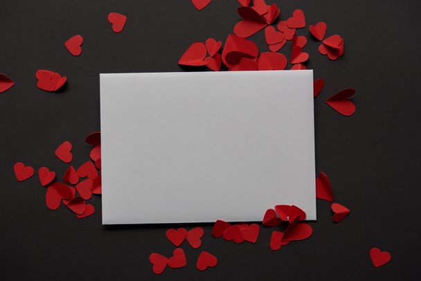 top view of white empty greeting card and red paper cut hearts on black background - Foto, imagen