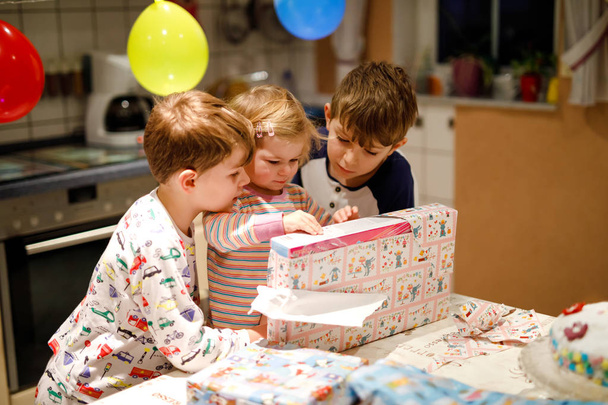 Adorable niñita celebrando su segundo cumpleaños. Niño bebé y dos niños niños desempacando regalos. Feliz niños sanos hermanos se sorprende acerca de grandes cajas y juguetes
 - Foto, imagen