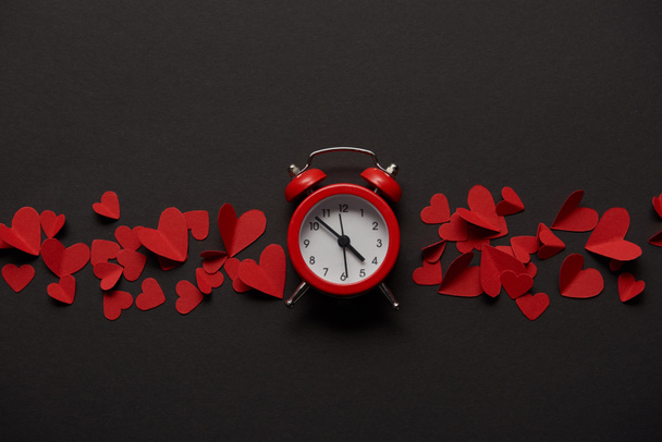 top view of clock and red paper cut decorative hearts on black background - Foto, immagini