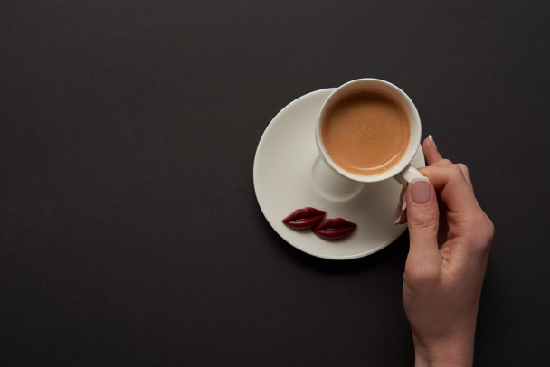 top view of woman holding cup of coffee near chocolate lips on saucer - Foto, Bild