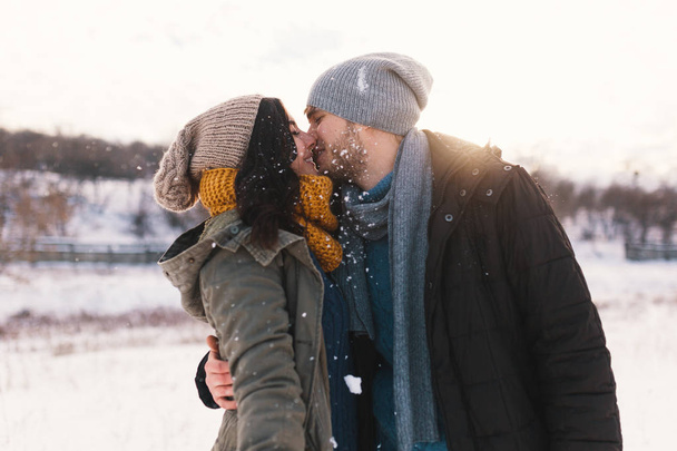 Happy woman and man, kissing, and huging, spending time together enjowing eachother, snow, life, winter. Portrait wonderful young couple wearing stylish wool hats and scarfs. - 写真・画像