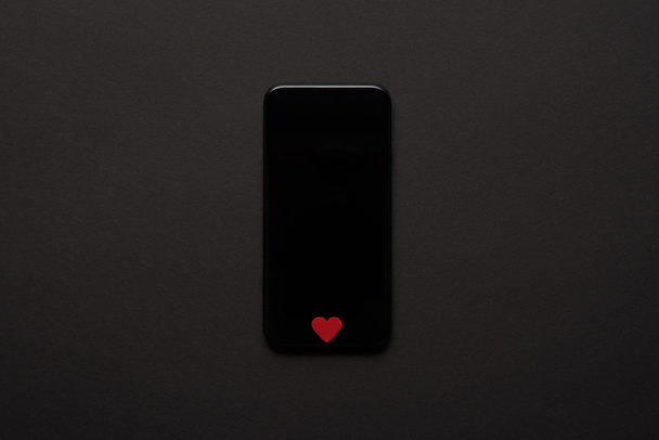top view of smartphone with blank screen and small red heart sign on dark background - Zdjęcie, obraz