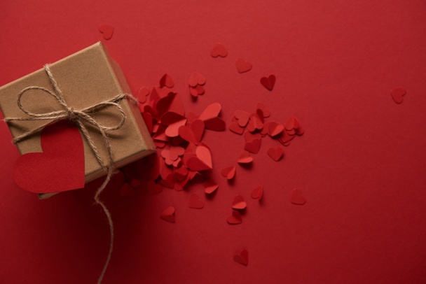 top view of decorative paper cut hearts and gift box with empty card on red background - 写真・画像